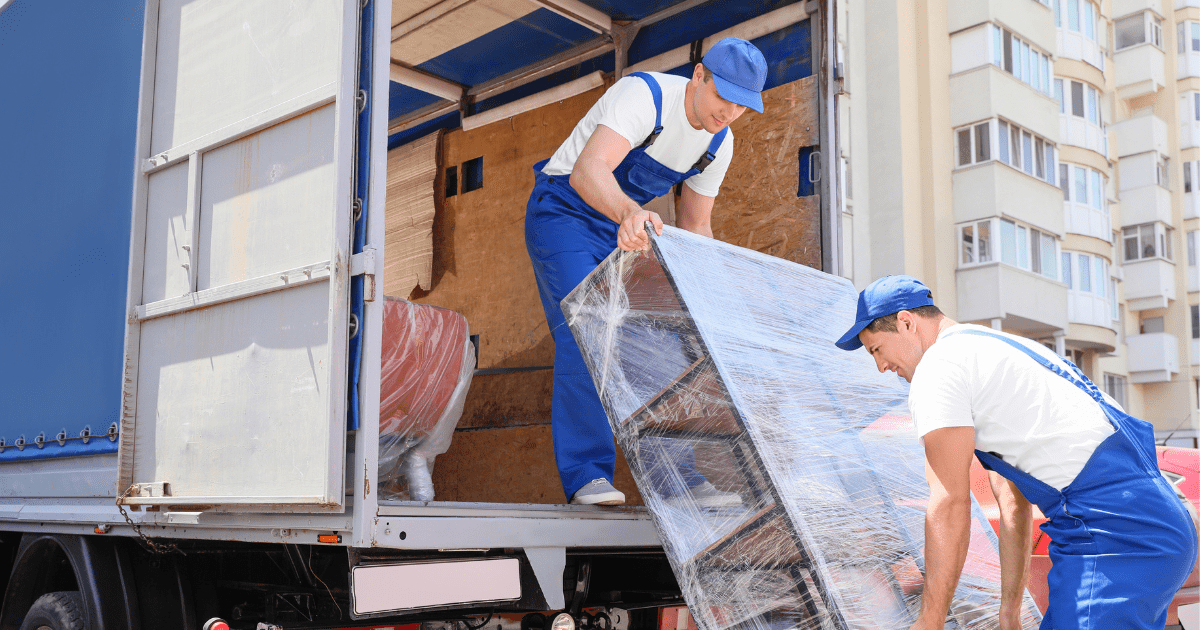 2 delivery man wearing blue jumpsuits carrying furniture