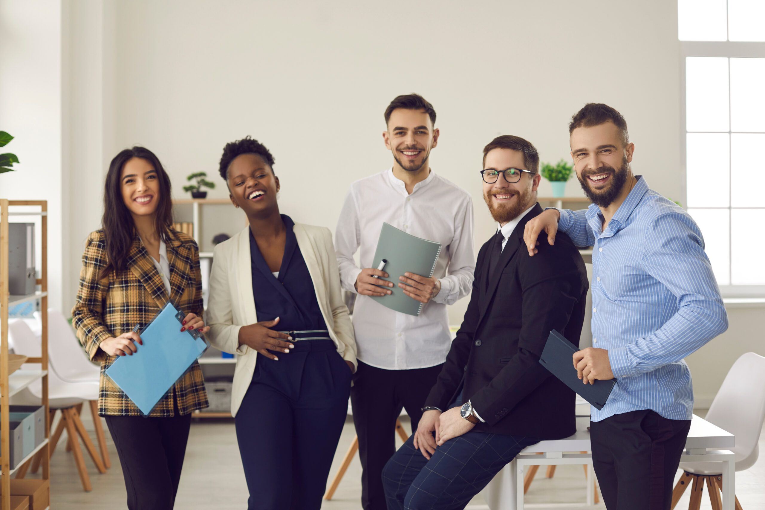 Unity, motivation and teamwork. Funny creative business team, diverse company representatives, interracial coworkers with paper documents standing together and laughing posing for office portrait